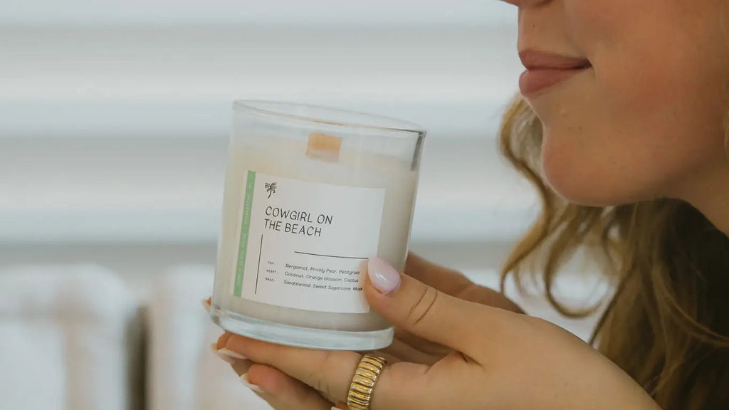 Woman holding a 'Cowgirl on the Beach' candle with a neutral background