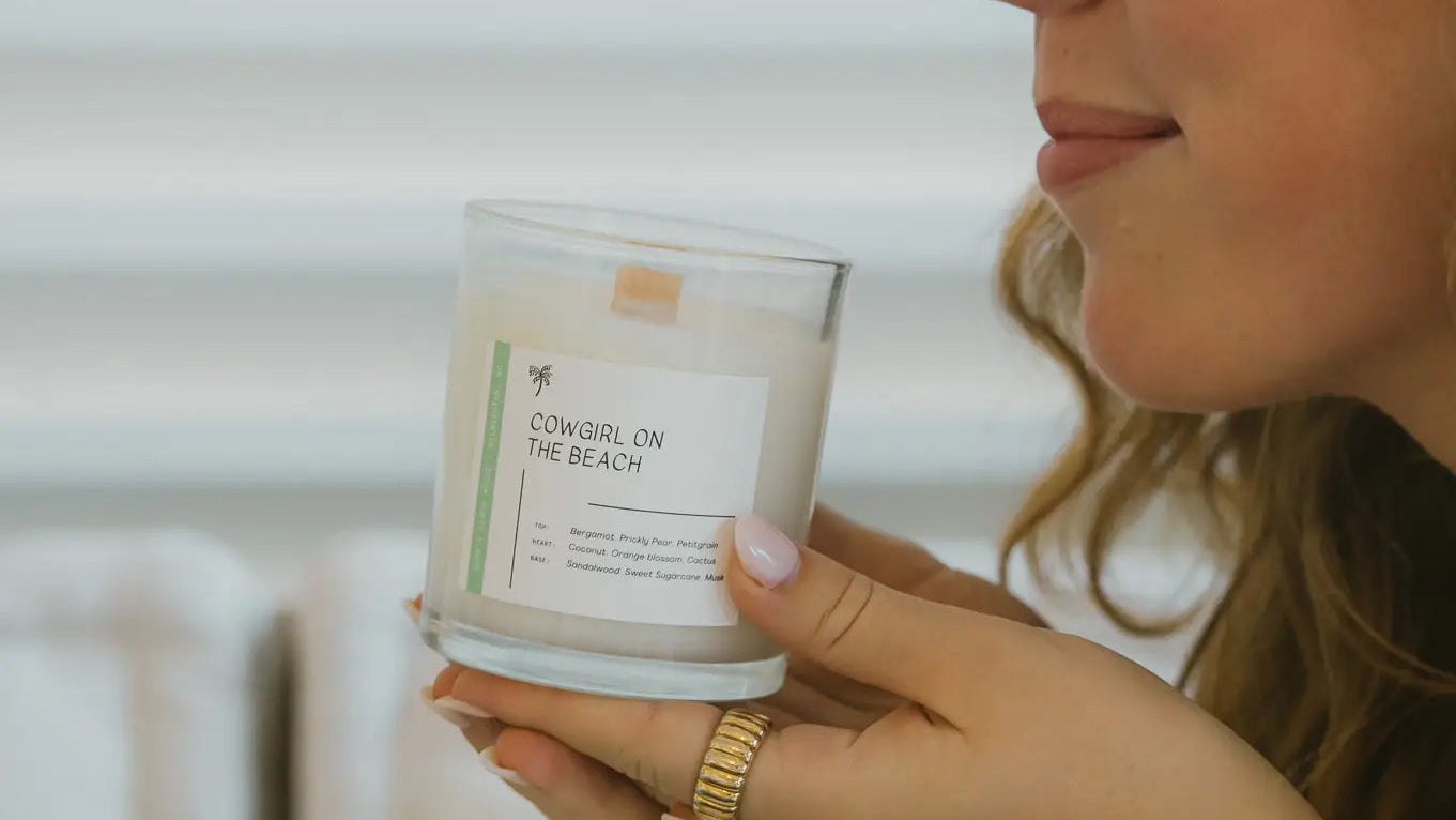 Woman holding a 'Cowgirl on the Beach' candle with a neutral background